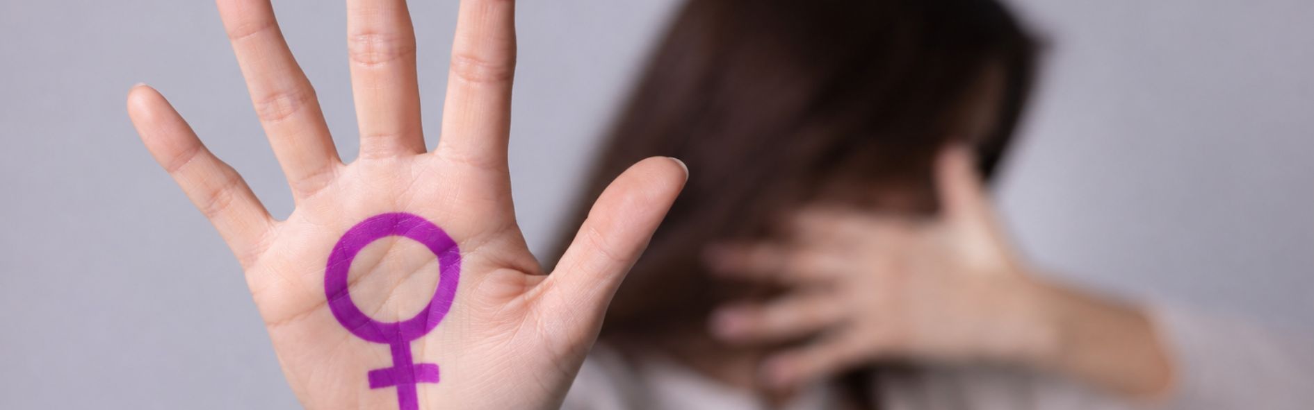 Prevención de violencia de género con mujer mostrando mano en señal de protección y símbolo feminista.